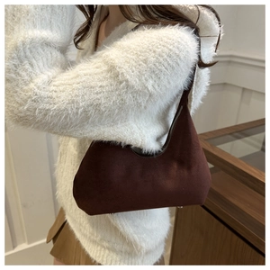 Detail of dark brown suede crescent bag worn with a cozy white sweater on shoulder