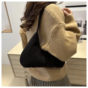 Detailed close-up of a black suede underarm bag with protective metal feet on the bottom