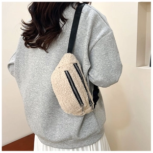 Detail of cream sherpa waist bag with black zippers and adjustable strap on a model