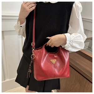 Detail of red leather trapezoid handbag with metal logo and woven charm accessory