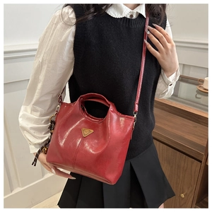 Red glossy leather bucket bag with metallic triangle logo and tassel on a model