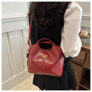 Detail of burgundy trapezoid bucket bag featuring a gold triangle plaque and smooth PU leather