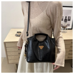 Detail of a black glossy bucket bag with golden triangle logo and woven bead charm detail