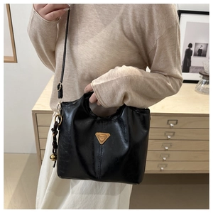 Detailed view of black leather bucket bag with gold triangular logo and woven charm accessory