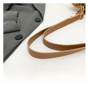 Detailed macro view of the brown leather shoulder strap with golden metal hardware and stitching
