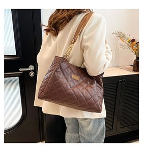 Detail of a brown quilted tote bag featuring faux leather texture and golden chain straps