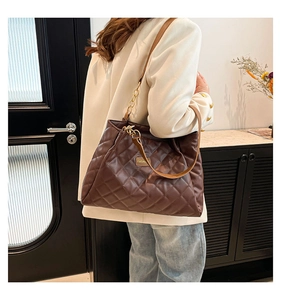 Detail of dark brown quilted crossbody bag featuring gold fashion plaque and chain strap