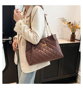Detail of coffee brown quilted tote bag with gold chain strap and metal fashion logo tag