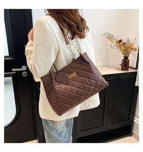 Detailed view of deep brown quilted tote bag with gold chain strap and metal logo plate