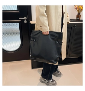Dettaglio della borsa tote minimalista in pelle nera con finitura opaca e manico superiore