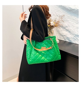 Detail of quilted green tote bag featuring golden metal chain and leather strap