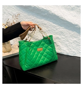 Detailed macro view of the green quilted leather texture and gold chain strap of the tote bag