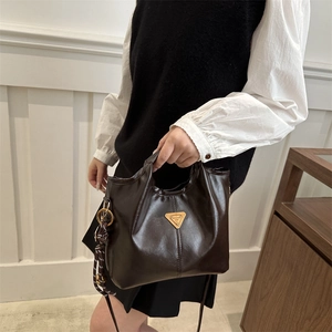 Minimalist dark brown polished leather bucket bag with gold triangle logo and woven charm