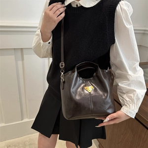Deep brown glossy bucket bag with golden triangle logo worn by model in minimalist style