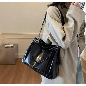 Close-up of black leather tote bag featuring a gold buckle and metal chain strap