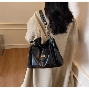 Detail of the black leather tote bag featuring a gold metal twist lock and chain strap