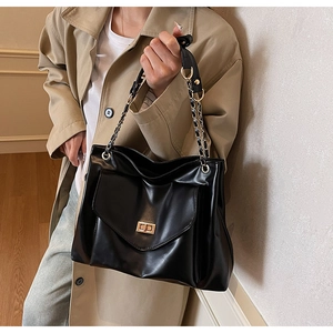 Detail of black faux leather tote bag showing gold turn-lock and chain strap