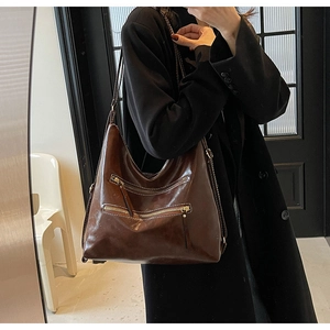 Détail de la texture en cuir marron brillant et des poches zippées du sac fourre-tout