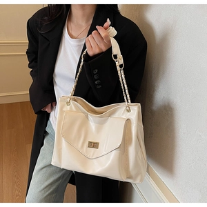 Close-up of cream tote bag with gold twist-lock pocket and metal chain shoulder strap