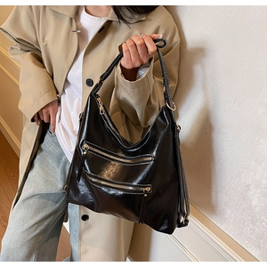 Détail du sac cabas en cuir noir brillant avec fermetures éclair dorées sur trench-coat