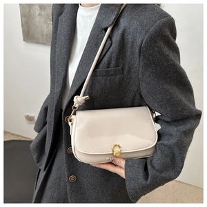 Detail einer cremeweißen Satteltasche mit rundem goldfarbenem Metallverschluss am Model