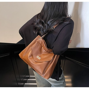 Rear view of a brown leather tote bag with gold chain strap worn on a staircase