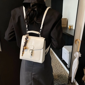 Elegant off-white square backpack with stylish buckle and brown woven charm accessory