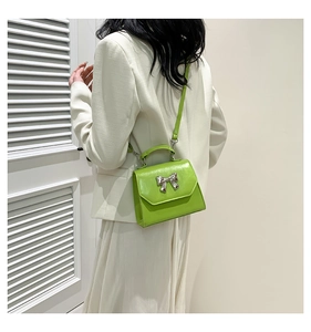 Detail of lime green glossy crossbody bag featuring a silver metal bow accent and top handle