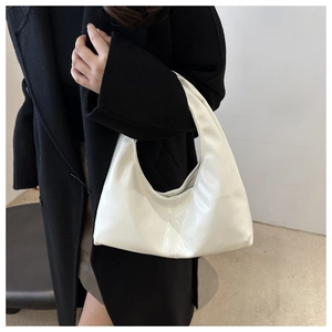 Close-up of a glossy white hobo bag shown on a model wearing a long black coat