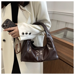 Detail of dark brown glossy patent leather hobo bag worn with a white blazer