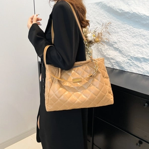Quilted light brown tote bag with metal chain strap worn by model in casual style