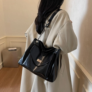 Black leather tote bag with gold twist lock and chain strap on a trench coat model