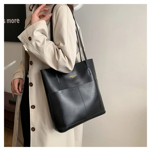 Detail shot of black faux leather tote bag with gold logo and decorative stitching on surface