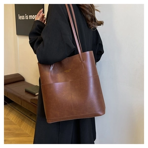 Nahaufnahme einer braunen Leder-Tote-Bag mit Goldschrift kombiniert mit schwarzem Mantel