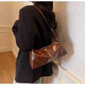 Brown oil wax leather underarm bag with metal rivets shown on a female model