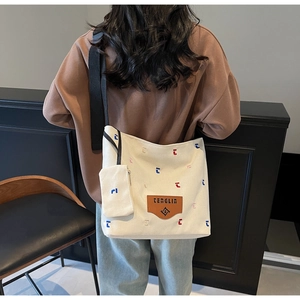 Detail of off-white canvas tote bag with letter embroidery and small side pouch