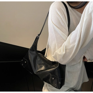 Detail of black glossy leather underarm bag with silver metal eyelets and rivets