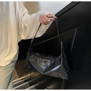Close-up of shiny black leather shoulder bag featuring silver rivet details and stitching