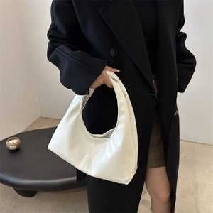 Minimalist white hobo bag in glossy leather held by a model in a modern interior setting