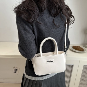 Minimalist white PU leather crossbody bag worn by model over a grey sweater and pleated skirt