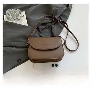 Brown leather crossbody bag with adjustable strap shown next to phone for scale