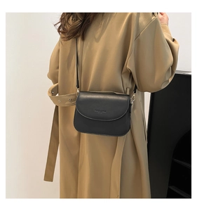 Detail of a black leather crossbody bag with a curved flap on a khaki trench coat