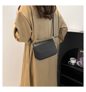 Detail of a black leather flap crossbody bag with gold metal hardware on a khaki trench coat