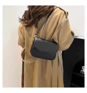 Close-up of a minimalist black saddle bag worn by a model in a modern casual style