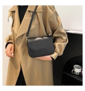 Close-up of matte black leather crossbody bag with gold hardware on a model in a trench coat