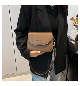 Close-up of caramel brown leather crossbody bag featuring fashion logo and golden hardware