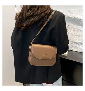 Detail view of the brown leather shoulder bag worn crossbody by a model in modern setting