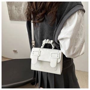 Detail view of white square messenger bag with a pleated handle and dual buckle design