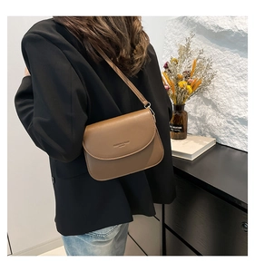 Brown leather crossbody bag with flap cover shown on shoulder in minimalist home setting