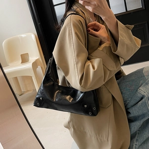 Minimalist black leather tote bag with silver metal studs worn over a khaki trench coat